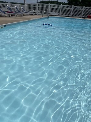 Ein klares Schwimmbecken mit weißem Zaun und Liegestühlen.