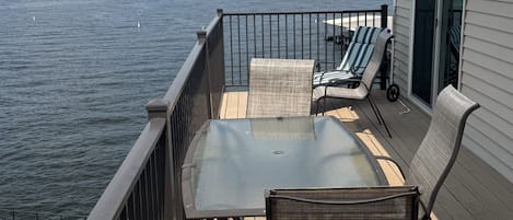 A deck with a table and chairs, overlooking a body of water with buildings in the distance.