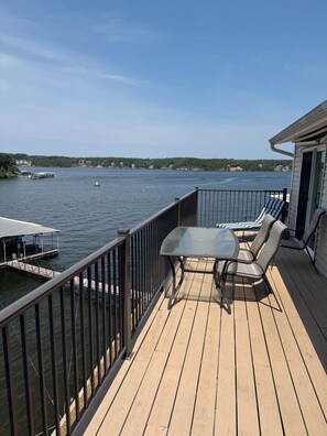 Eine Holzterrasse mit Tisch und Stühlen, mit Blick auf einen See, auf dem Boote fahren, und Häuser sind in der Ferne zu sehen.