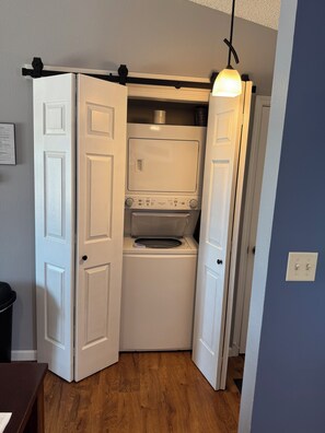 A compact laundry room with a washer and dryer, a hanging light fixture, and a door leading to another room. - NEWLY LISTED! The Perfect View of the Lake! (Osage Beach)