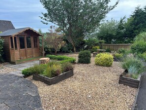 A garden with a wooden shed, a picnic table, and various plants. - Newly renovated cosy coastal retreat within walking distance of village pub! (Kippford)