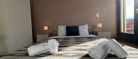 Une chambre d’hôtel avec un lit, deux tables de chevet, une armoire et une fenêtre donnant sur un beau paysage.