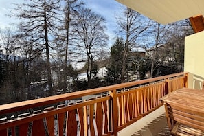 A wooden balcony with a view of leafless trees and a building in the background. - Luxury Apartment in Crans-Montana! (Crans-Montana)