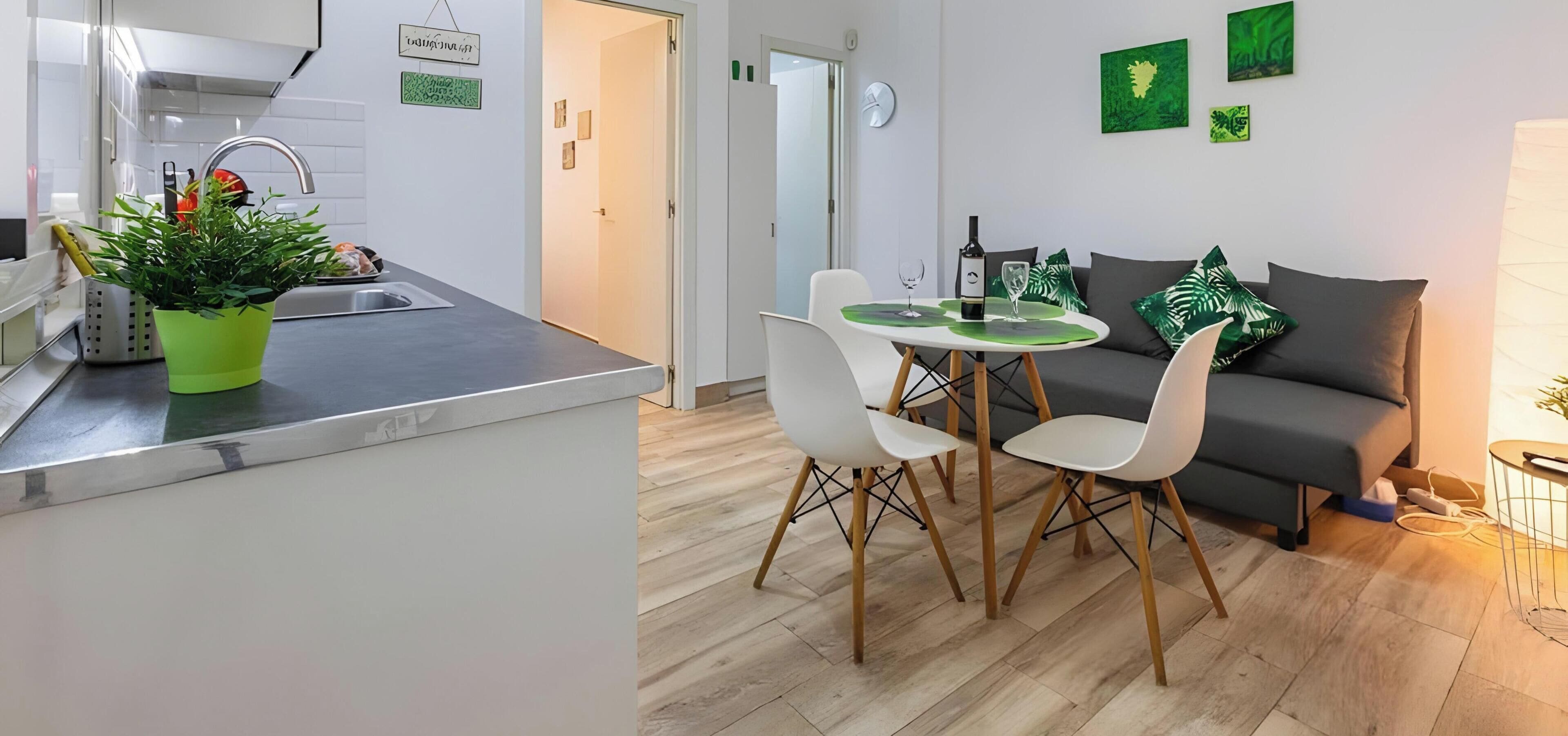 A modern kitchen with a sink, a dining table with chairs, and a grey sofa in a living area.