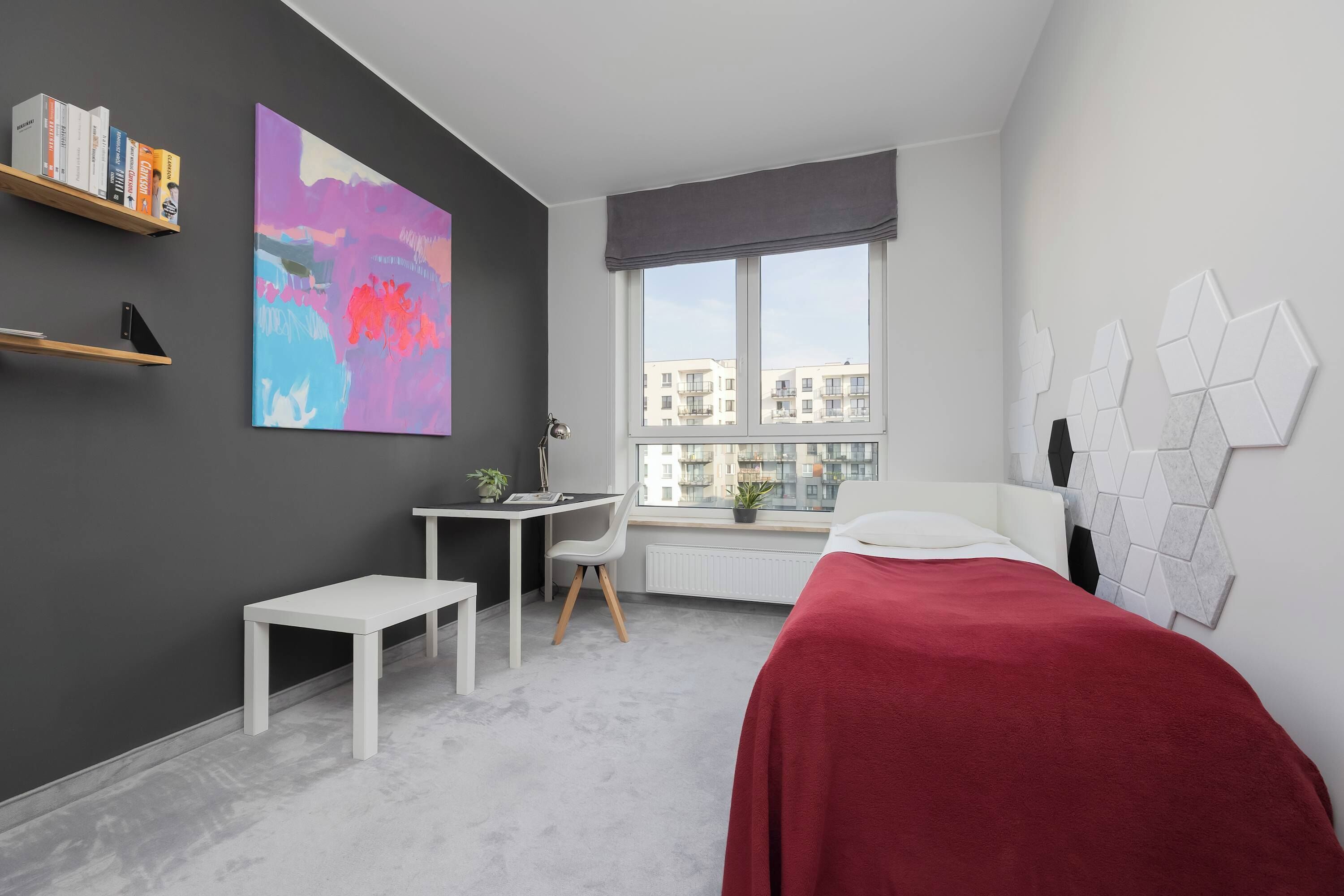 Ein modernes Schlafzimmer mit Bett, Schreibtisch, Stuhl, Fenster und Kunstwerken an den Wänden.