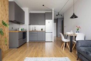 A modern kitchen with grey cabinets, a white refrigerator, and a wooden countertop. There is a dining area with a table, chairs, and a grey sofa. - Spacious Flat with a Balcony | Parking | Air-conditioning (Warszawa)