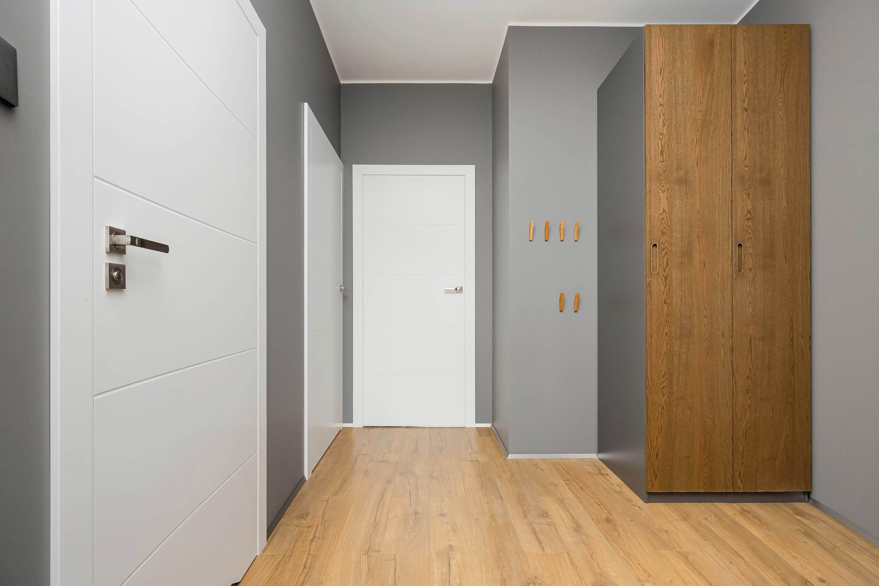 A hallway with a wooden floor, white walls, and a wooden wardrobe.