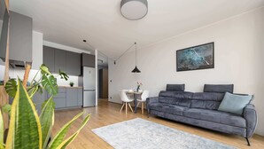Un espace de vie moderne comprenant un canapé gris, une table à manger avec des chaises, un coin cuisine et une grande fenêtre.