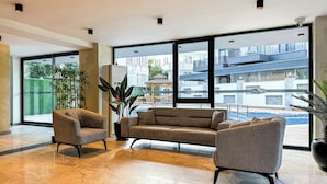 A modern hotel lobby with a large window, a sofa, two armchairs, and a potted plant. - Qoople Elite 2 City B1 - Cozy 1-bedroom apartment in Alanya (Alanya)