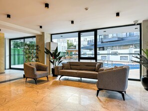Eine moderne Hotelhalle mit großem Fenster, einer Couch, zwei Sesseln und einer Zimmerpflanze.