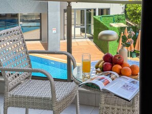 Ein Korbstuhl, ein Glas Saft und eine Obstschale mit Äpfeln und Orangen auf einem Tisch.