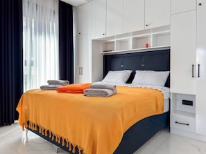 Ein modernes Schlafzimmer mit einem Bett, einem weißen Kleiderschrank und einem Fenster mit Vorhängen.