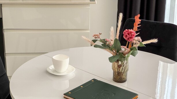 A round white table with a white cup, a green book, and a vase with flowers. - Qoople Elite 2 City B1 - Cozy 1-bedroom apartment in Alanya (Alanya)