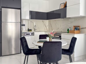 Eine moderne Küche mit einem Einbaukühlschrank, einem Geschirrspüler und einem Herd. Ein Esstisch mit zwei Stühlen und eine Vase mit Blumen sind ebenfalls vorhanden.