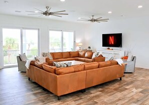 A spacious living room with a large sectional sofa, ceiling fans, a flat-screen TV, and a balcony view. - Atlantis: Largest Pool, Spa, Game Room, Fire Pit, 2 Min to Beach, Beach Gear (Miramar Beach)