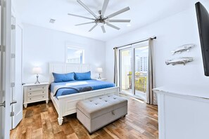 Un dormitorio con cama, mesitas de noche, ventilador de techo, ventana con vistas y puerta corredera.
