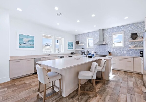 A modern kitchen with a large island, white cabinetry, and a patterned backsplash.