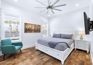 A bedroom with a bed, a chair, a nightstand, a ceiling fan, and a painting.
