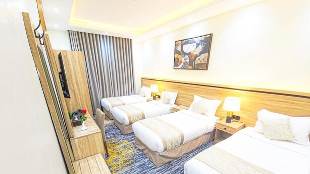 A hotel room with two beds, a wooden nightstand, a desk, and a wall-mounted TV. - Romance AlBadr Hotel (Makkah)