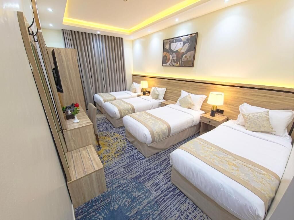 Habitación de hotel con tres camas, un aparador de madera, un cuadro grande en la pared y una alfombra estampada.