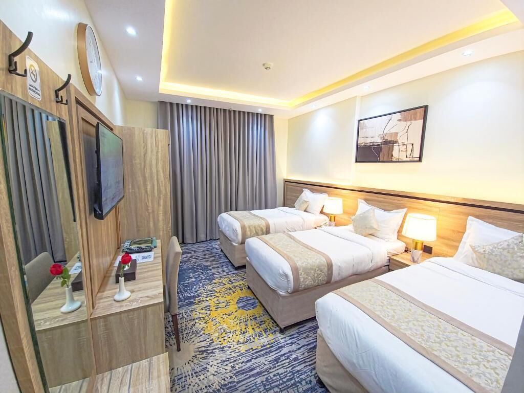 A hotel room with two beds, a desk with a chair, a TV, and a clock on the wall.