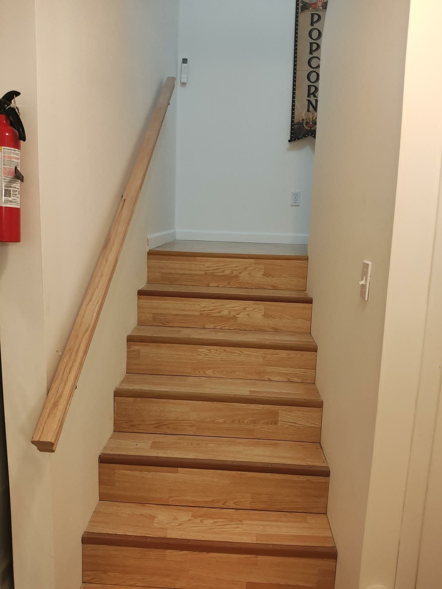 A wooden staircase with a handrail, a fire extinguisher, and a wall-mounted electrical outlet.