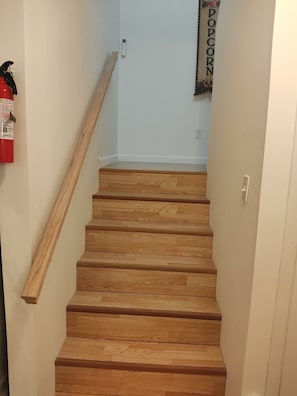 Een houten trap met een leuning, een brandblusser en een stopcontact op de muur.