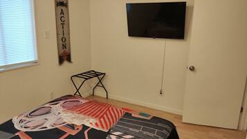Quarto com cama, TV fixada na parede e janela com persianas.