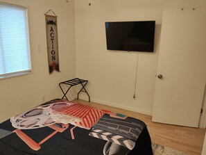 Un dormitorio con cama, televisión instalada en la pared y ventana con persianas.