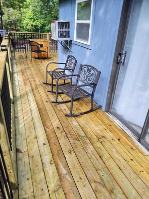 Una terraza de madera con sillas mecedoras de metal y una parrilla.
