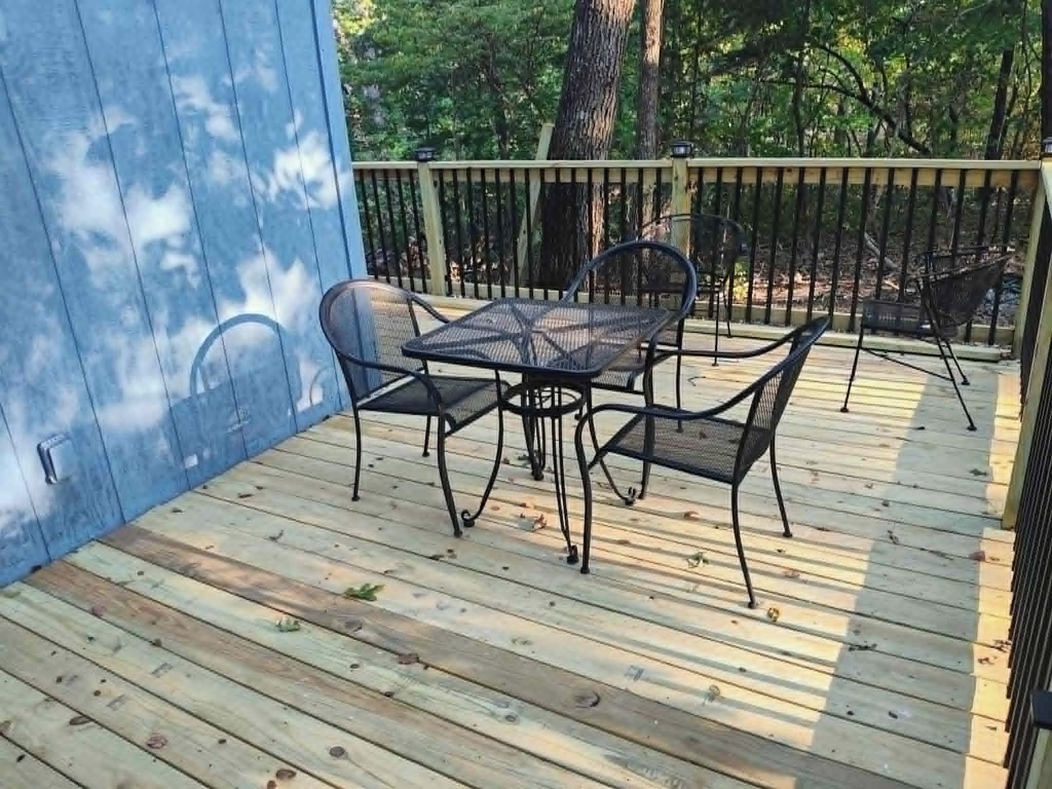 A wooden deck with a metal table and chairs, surrounded by trees.
