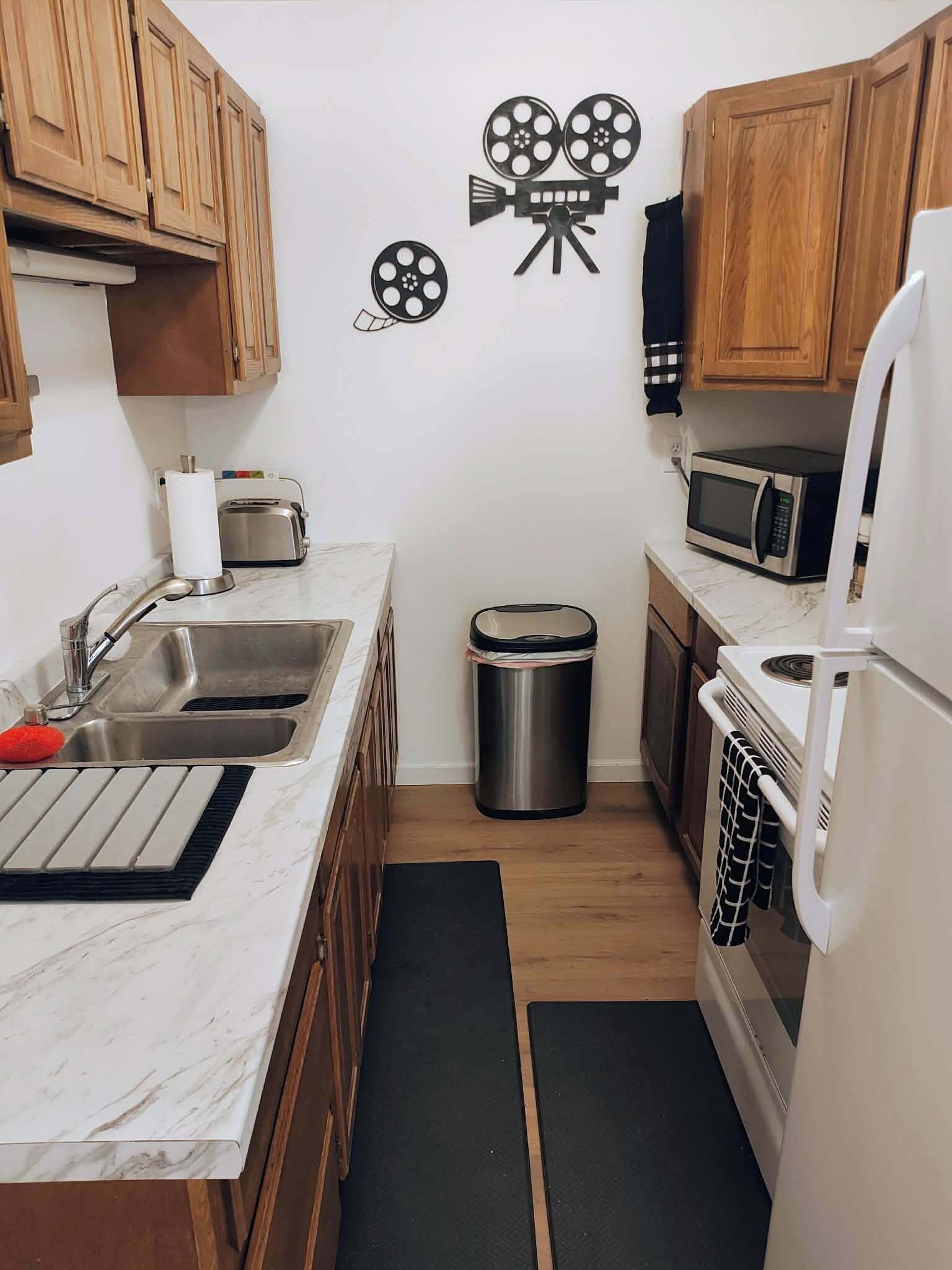 A kitchen with wooden cabinets, a stainless steel sink, a trash bin, a microwave, and a refrigerator.