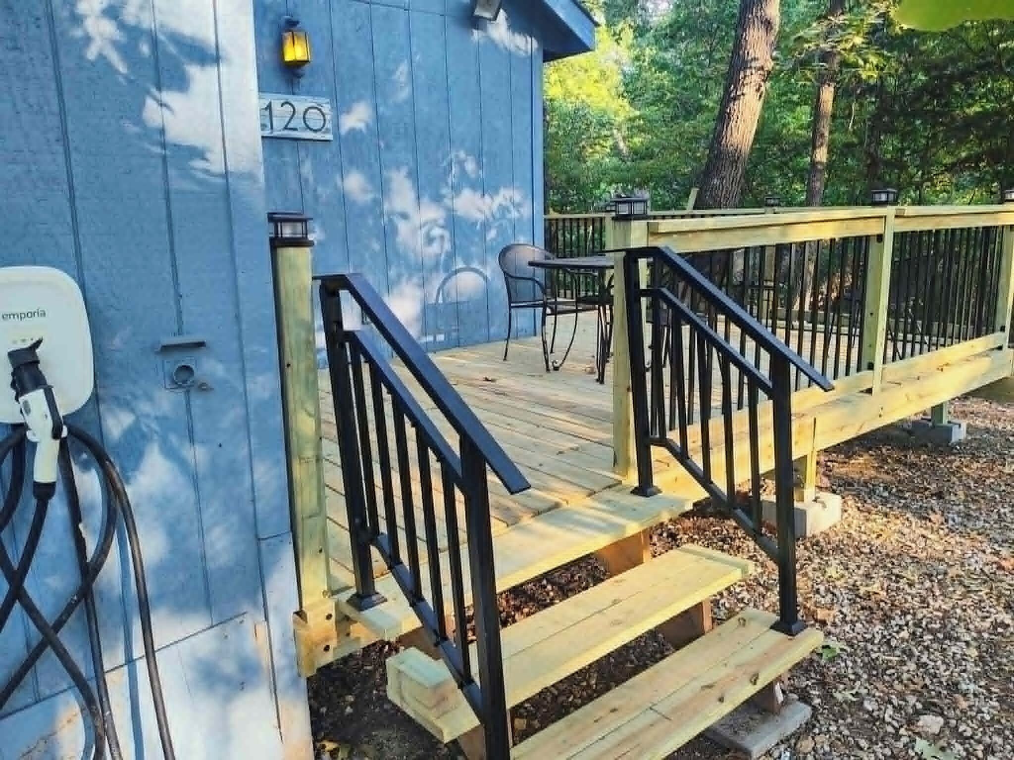 Une terrasse en bois avec une rambarde noire qui mène à un bâtiment à l’extérieur bleu, sur lequel on peut voir le numéro « 120 ».