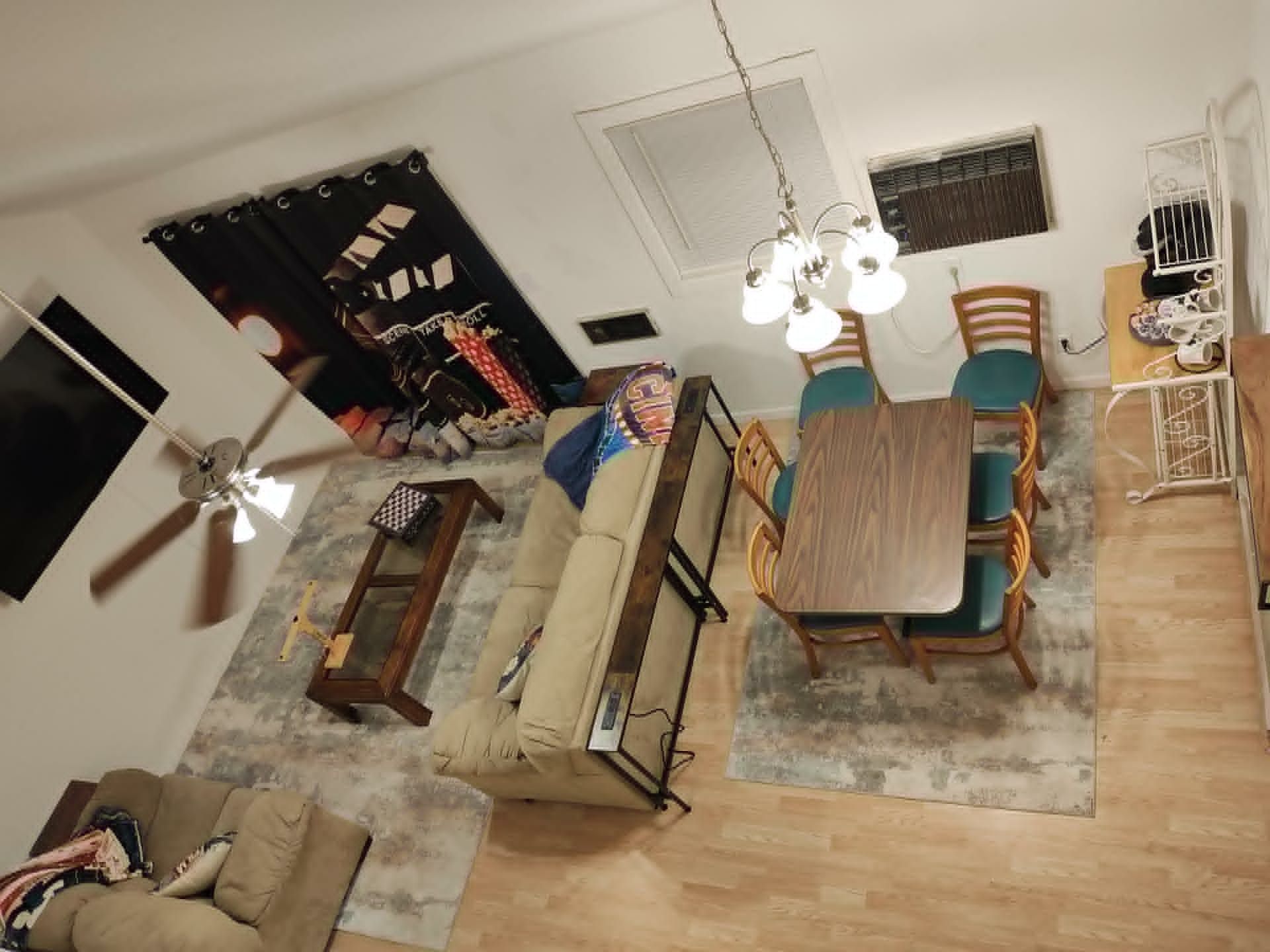 A room with a dining table, chairs, a sofa, a ceiling fan, and a window with blinds.