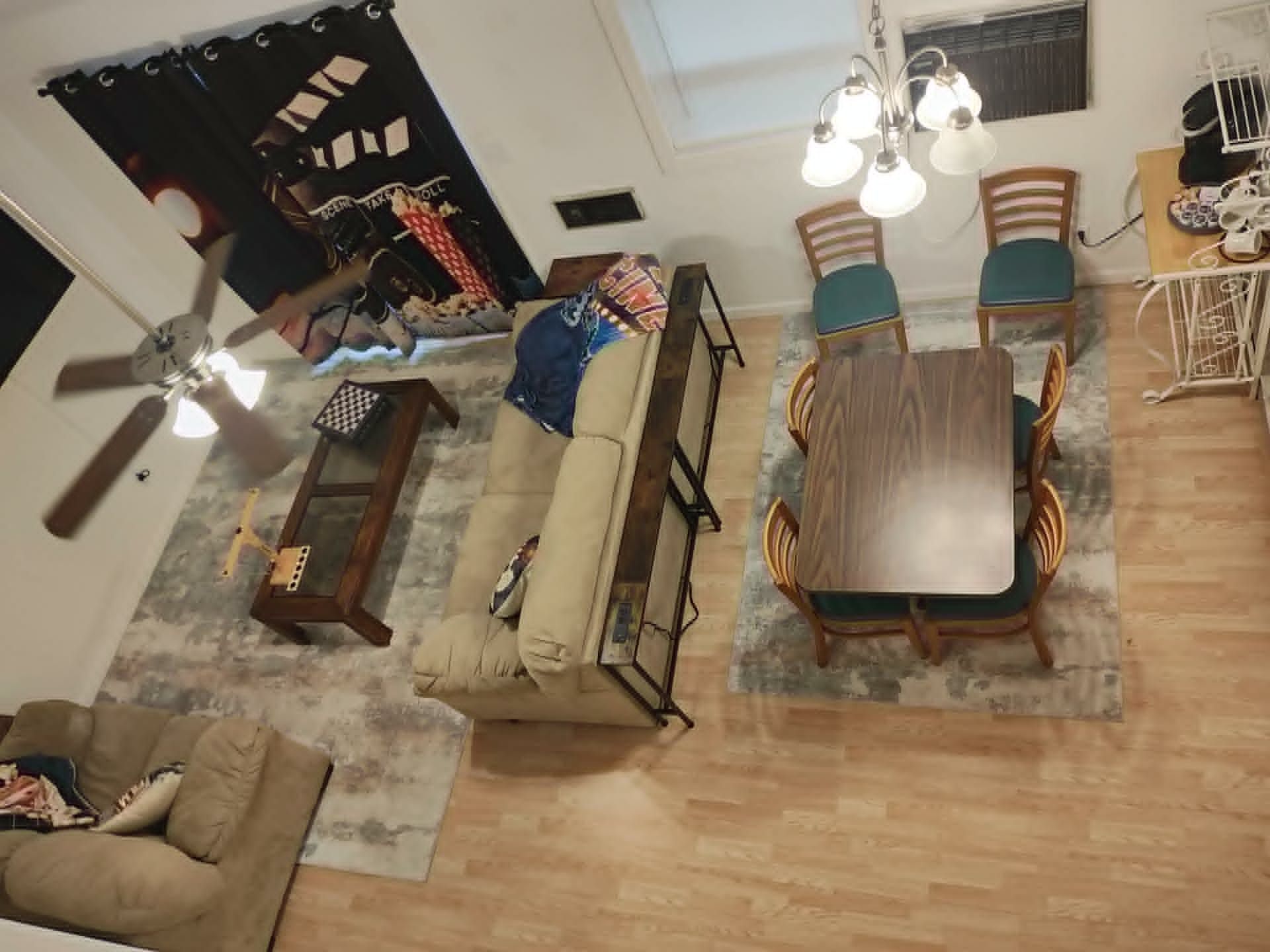 A living room with a sofa, a coffee table, a dining table with chairs, a ceiling fan, and a chandelier.
