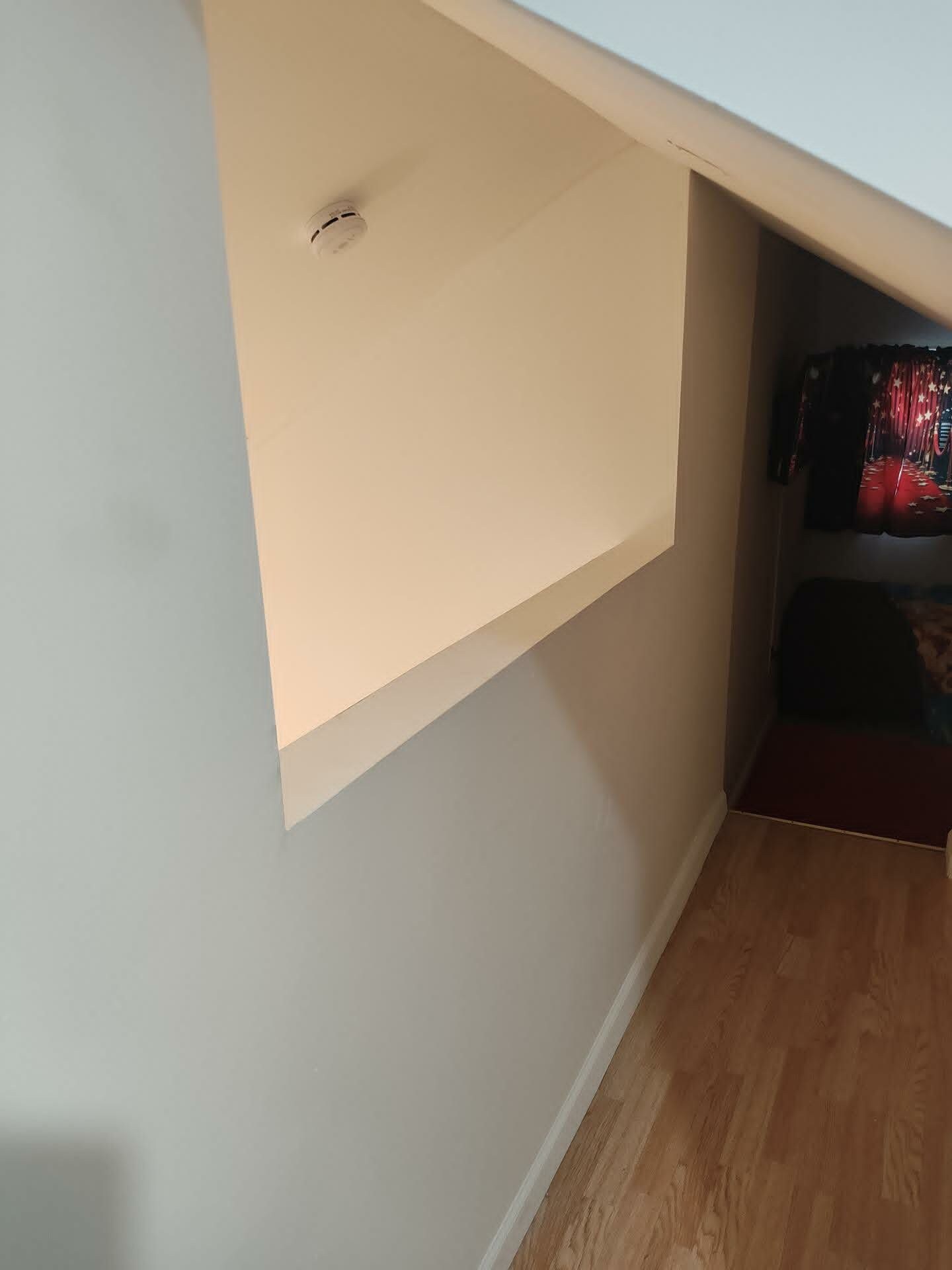 A room with a slanted ceiling, a visible smoke detector, and a partial view of a curtain with a star pattern.