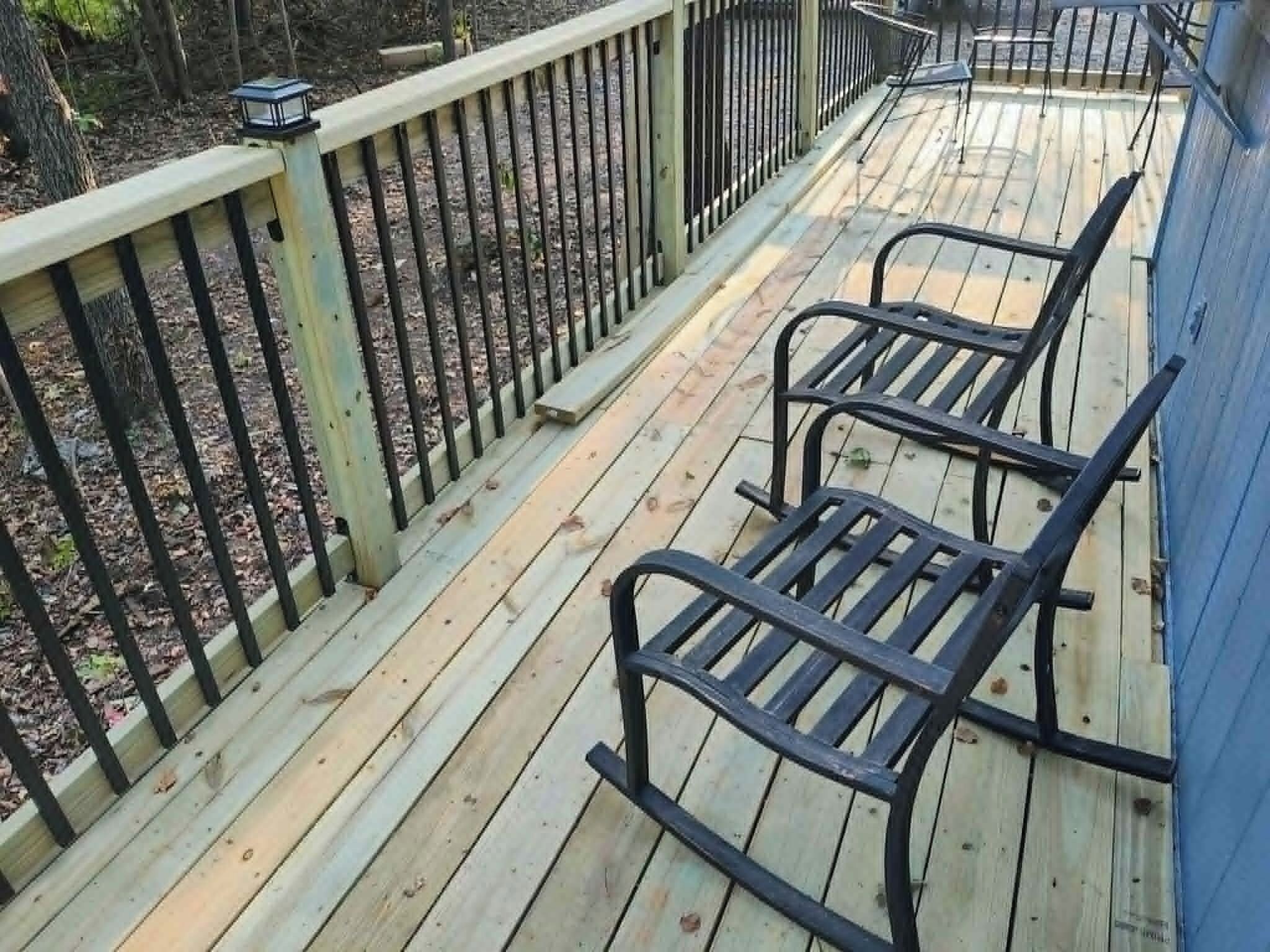 A wooden deck with metal railings and two rocking chairs.
