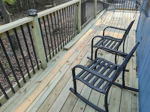 Een houten terras met metalen hekwerk en twee schommelstoelen.