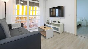 Ett modernt vardagsrum med en soffa, ett soffbord, en tv och en balkong med gula räcken.
