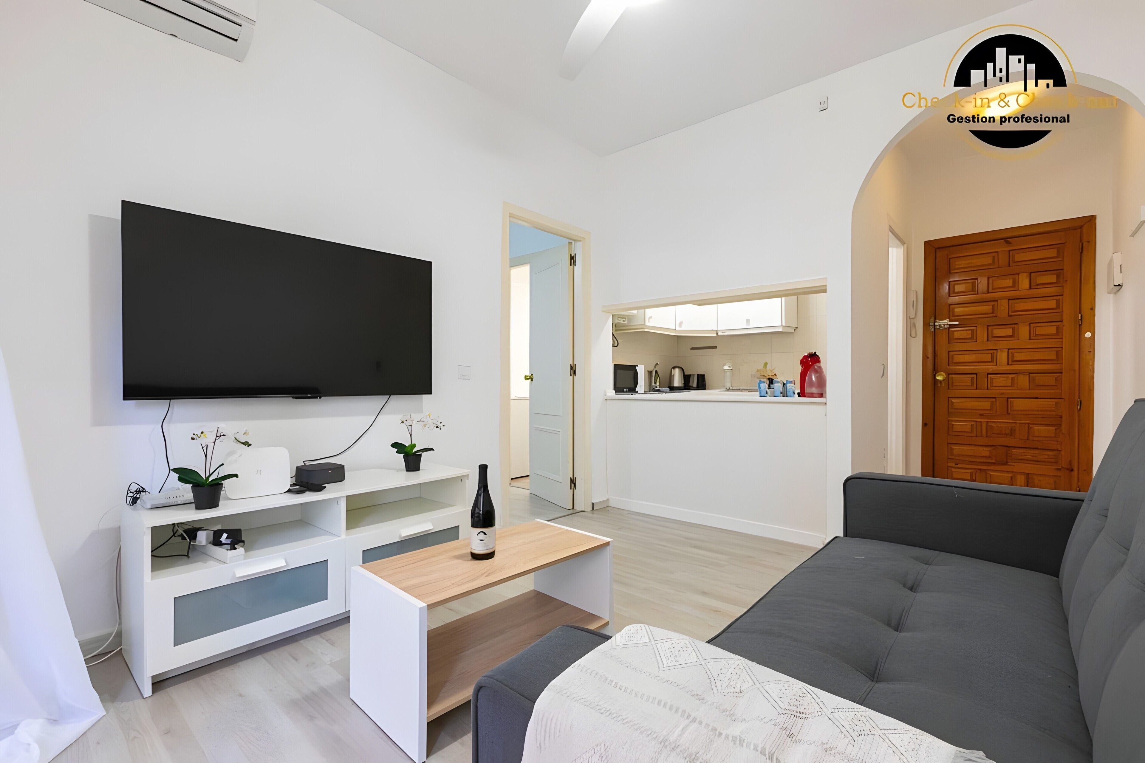 Ein modernes Wohnzimmer mit Flachbildfernseher, einem grauen Sofa, einem Holztisch und einer weißen Unterhaltungsecke.