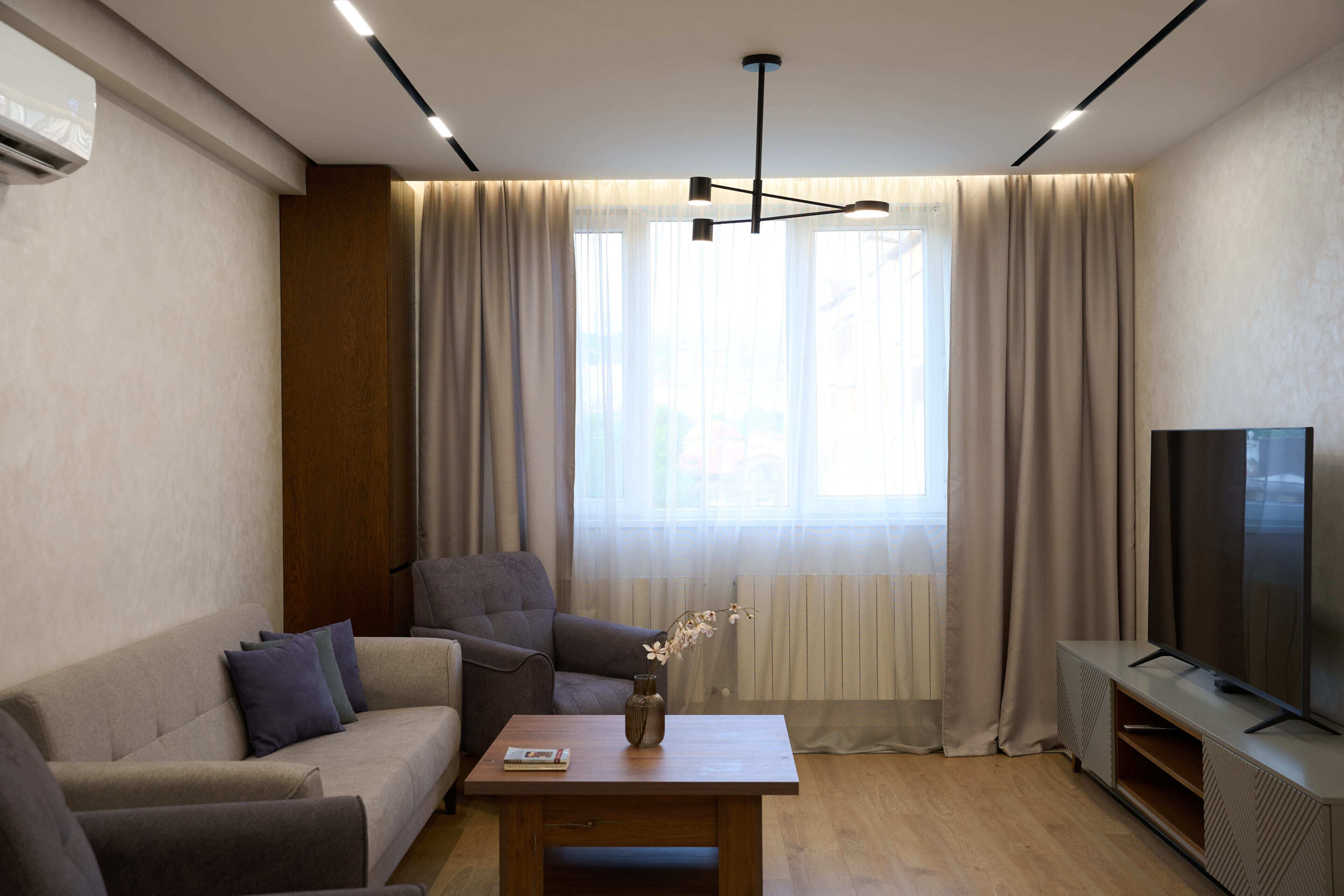 A modern living room with a sofa, a coffee table, a TV stand, and a large window with curtains.