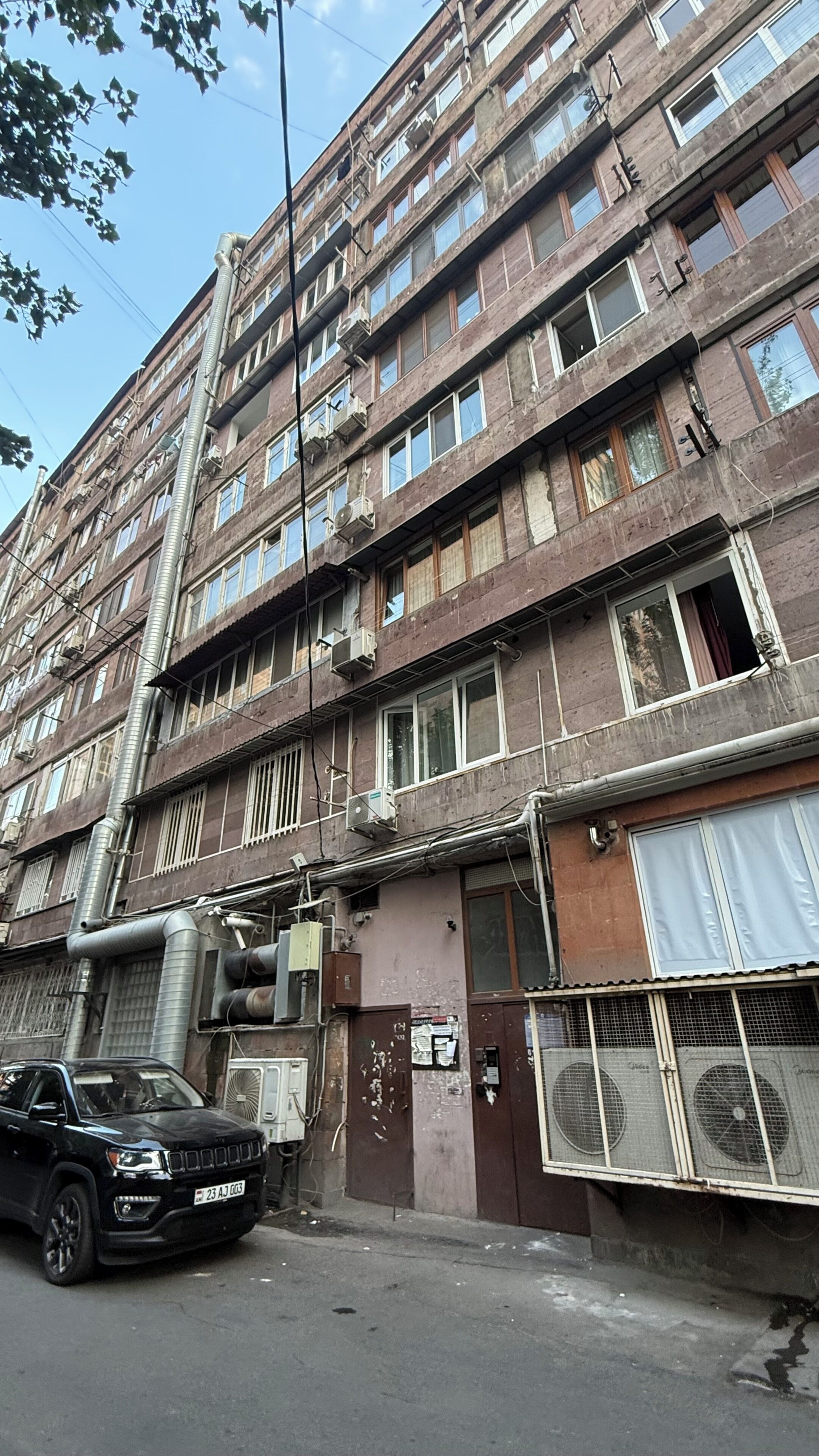 A multi-story building with air conditioning units, a parked car, and a gated entrance.