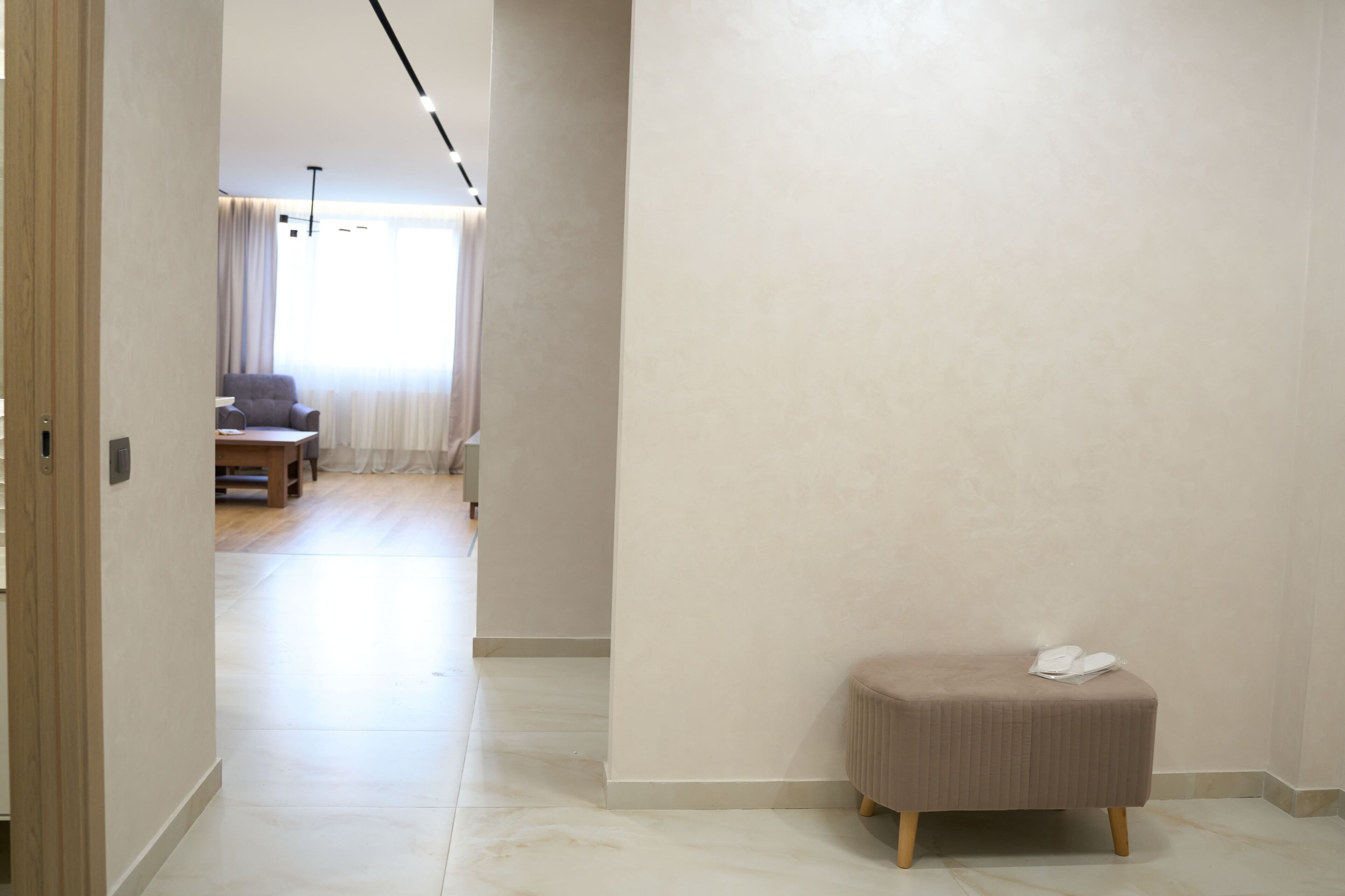 A hallway with a bench, a door, and a view into a living area with a sofa and curtains.