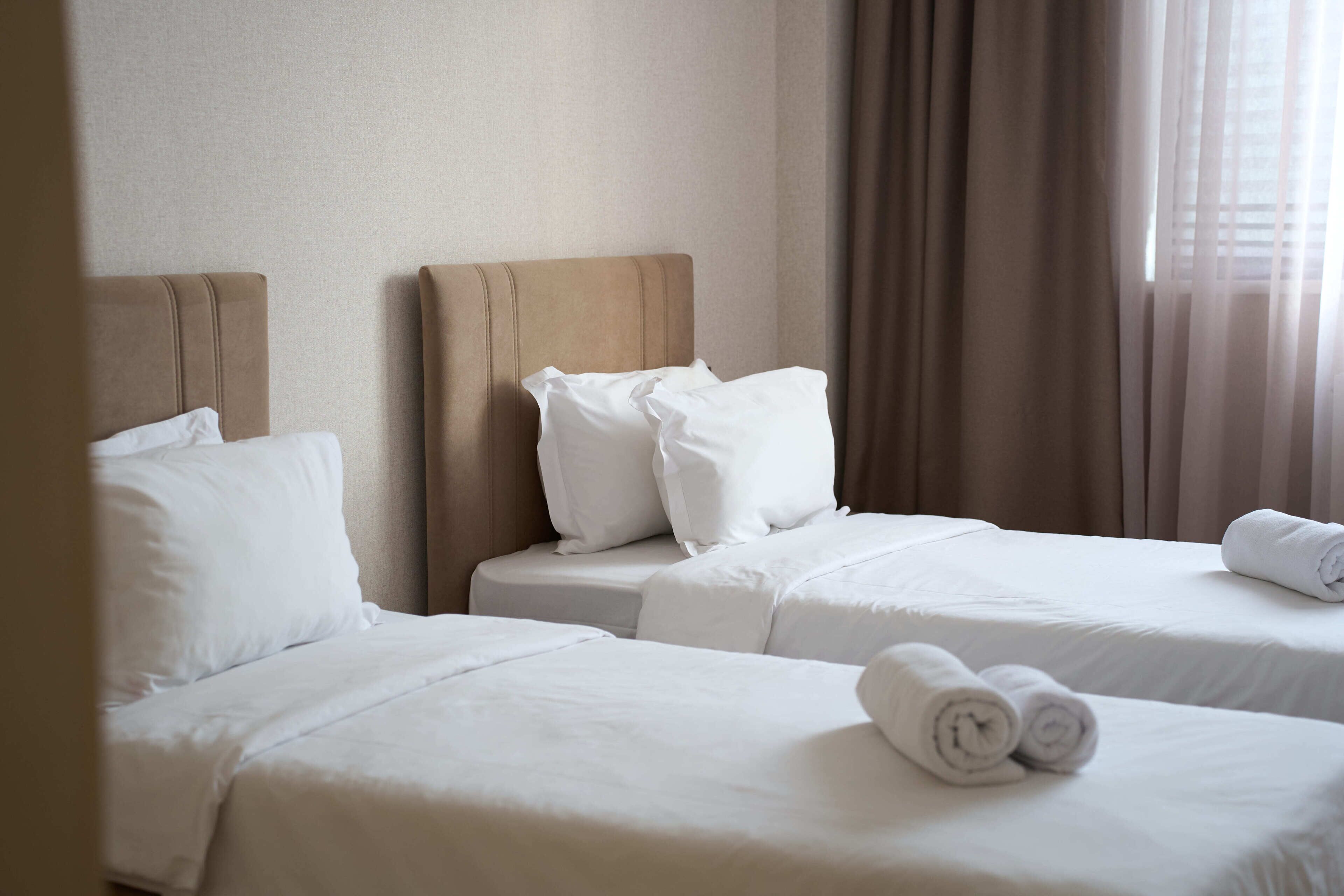 A hotel room with two beds, each with white bedding and pillows, and a neatly made towel on the bed.