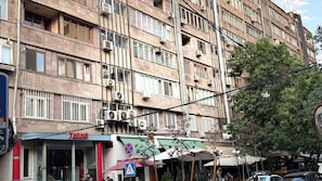 Un edificio de varios pisos con unidades de aire acondicionado, un local comercial con un letrero y una señal de paso para peatones.