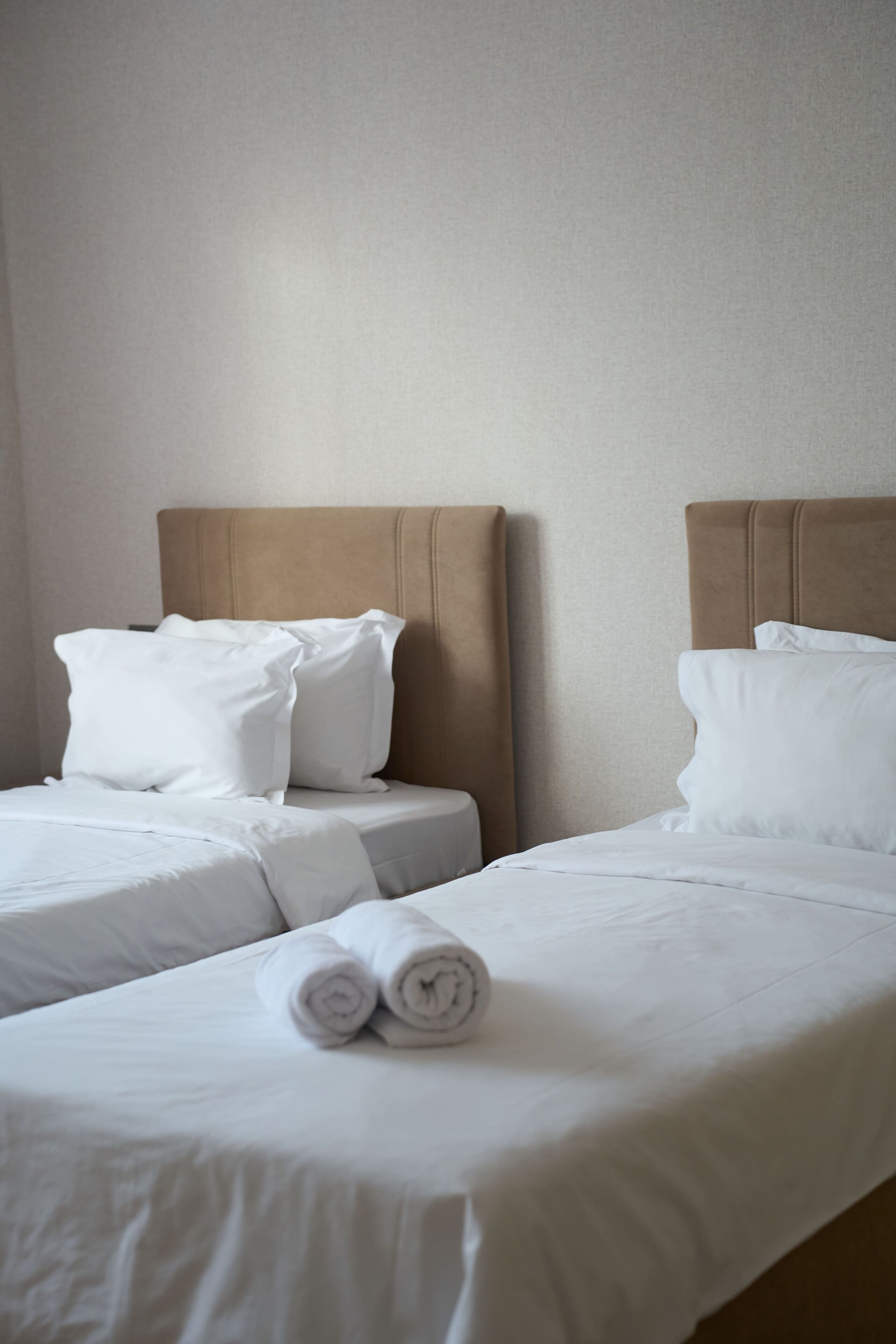 A hotel room with two beds, each with white linens and pillows, and a headboard.