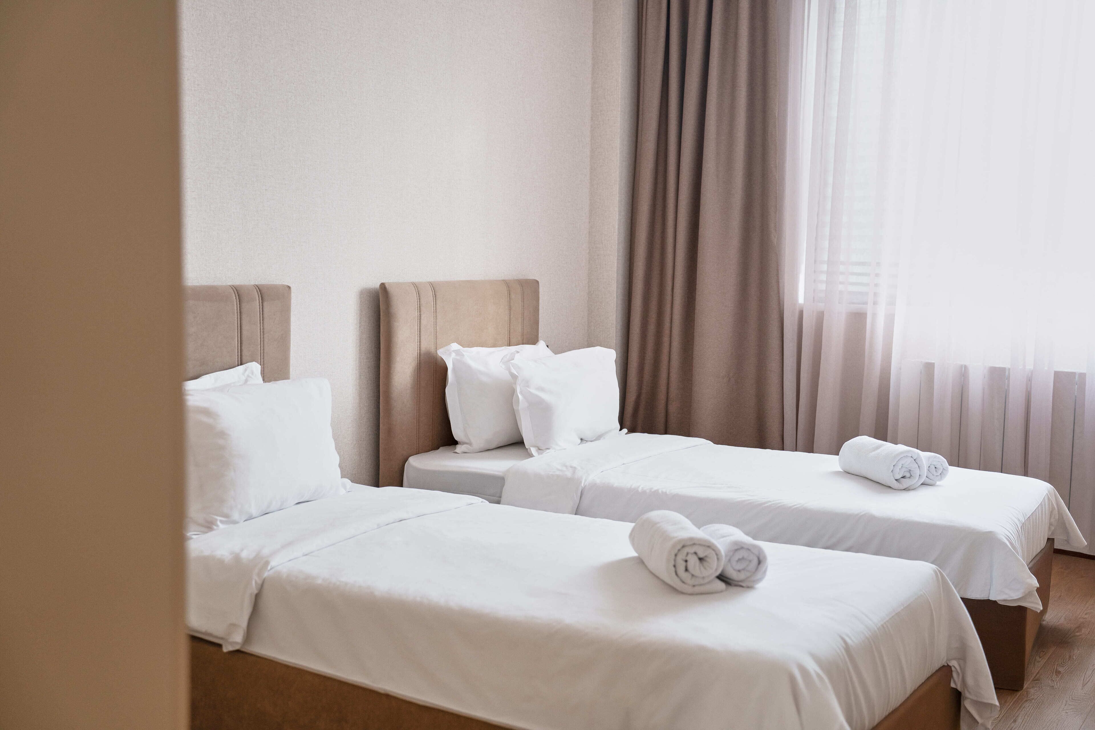 A hotel room with two single beds, each with a pillow and a rolled towel.