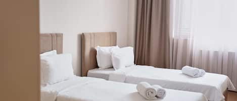 Ein Hotelzimmer mit zwei Einzelbetten, jeweils mit einem Kopfkissen und einem zusammengerollten Handtuch.