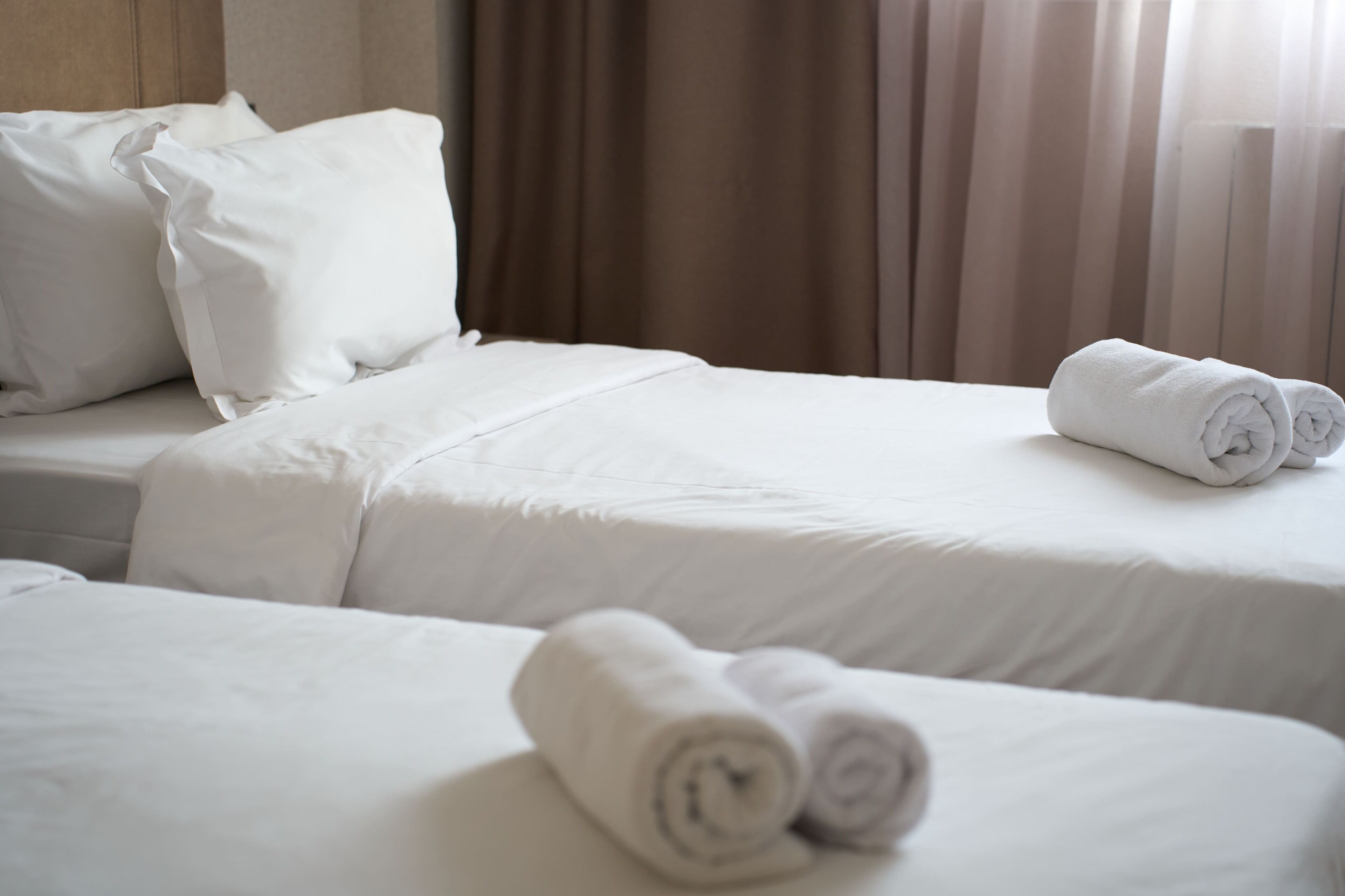Een hotelkamer met twee bedden, elk voorzien van witte lakens en kussens, en een opgerolde handdoek op de vloer.