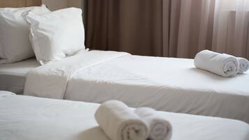 Een hotelkamer met twee bedden, elk voorzien van witte lakens en kussens, en een opgerolde handdoek op de vloer.